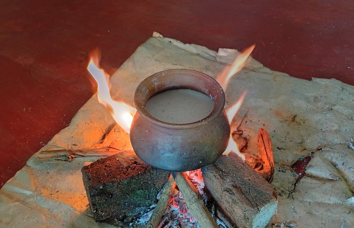 Clay pot with liquid sits on a wood fire pit, flames licking around the pot on a stone surface.